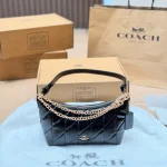 This underarm bag features shiny cowhide leather, in a classic black colorway with a metal chain-box